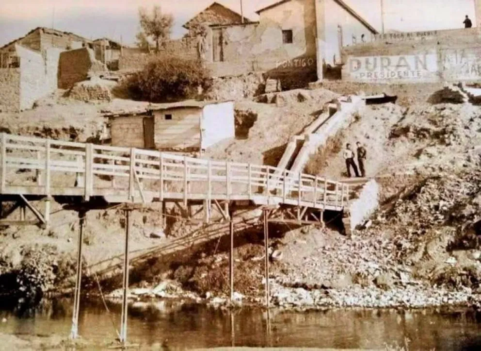 En la imagen se aprecia una estructura de madera utilizada como puente peatonal la que fue derribada varias veces por el caudal del río antes de que se construyere el puente El Libertador.
